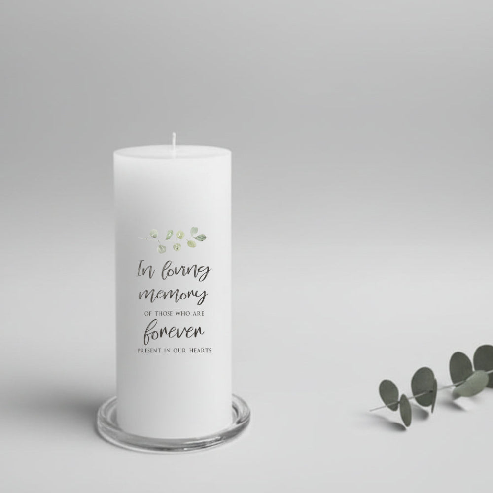 A white pillar candle printed with memorial text on a glass plate holder and a neutral background.