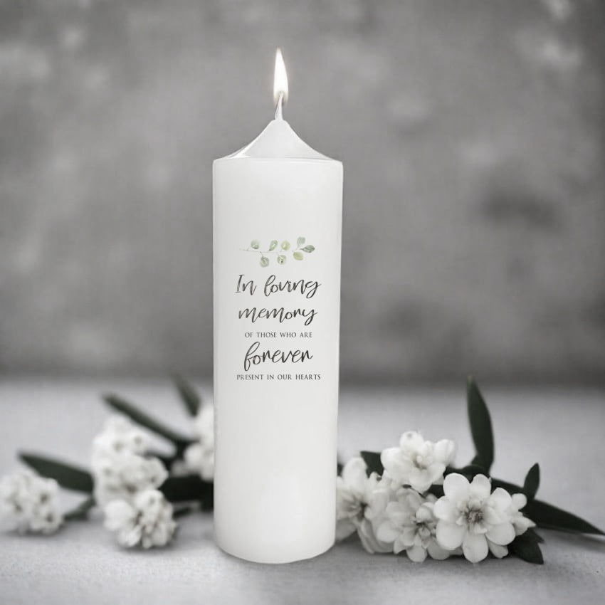 White memorial candle with text 'In loving memory of those who are forever present in our hearts' on a gray background with flowers.
