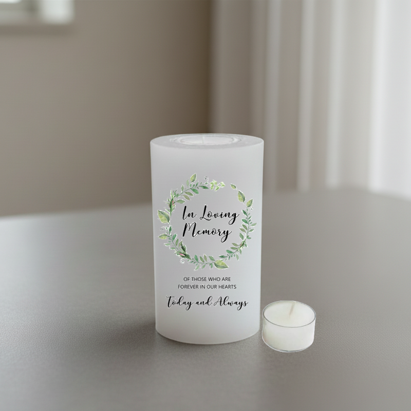 A white memorial candle with a green watercolor floral wreath and the words 'In Loving Memory' printed on the front