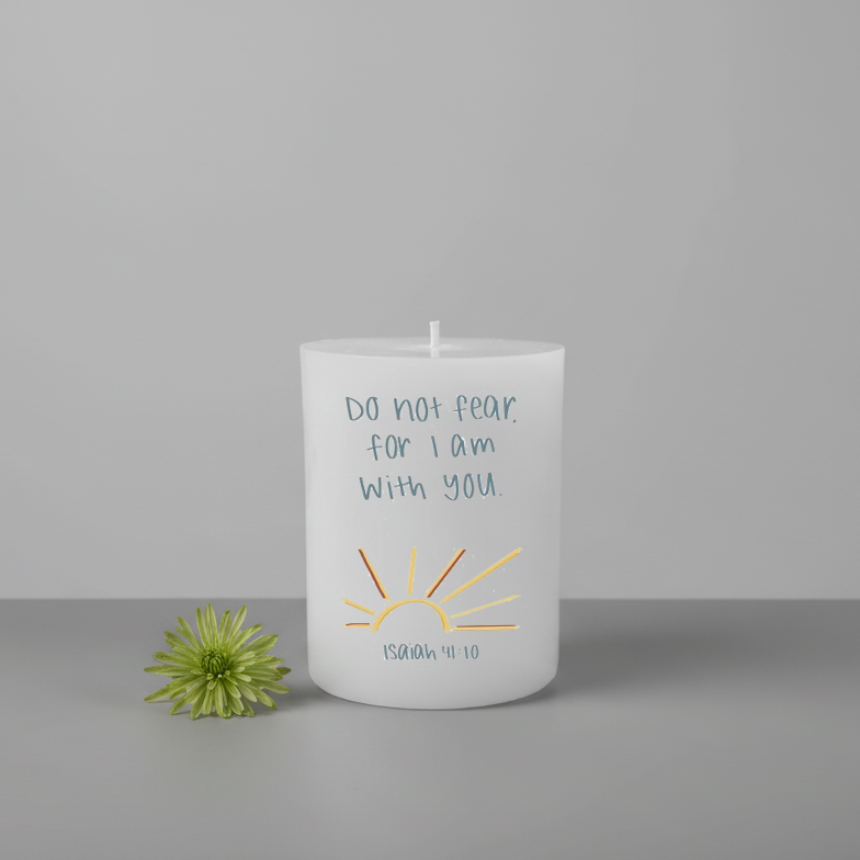 White candle with text and sun design next to a green flower on a gray background