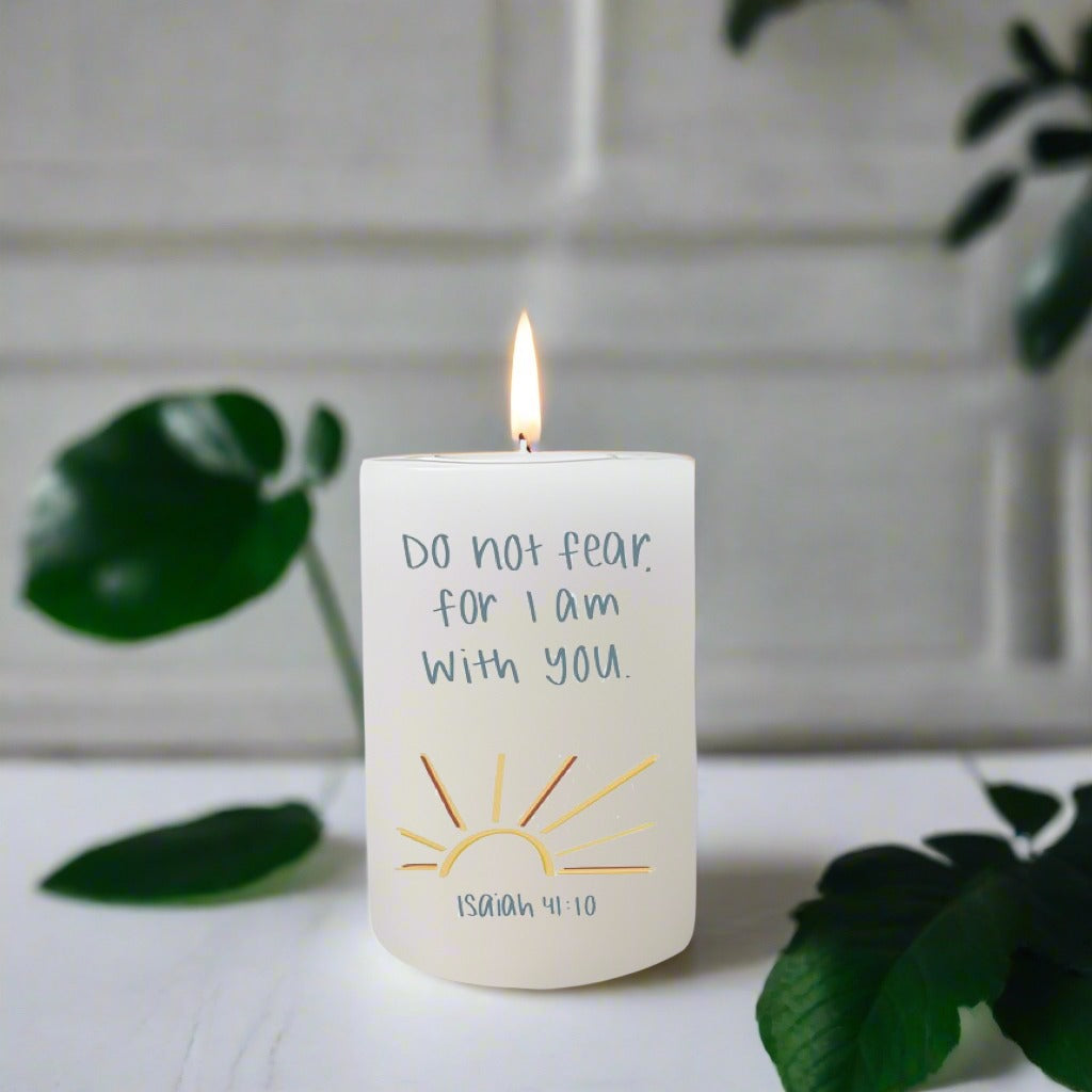 Candle with a motivational quote on a white surface with green leaves in the background