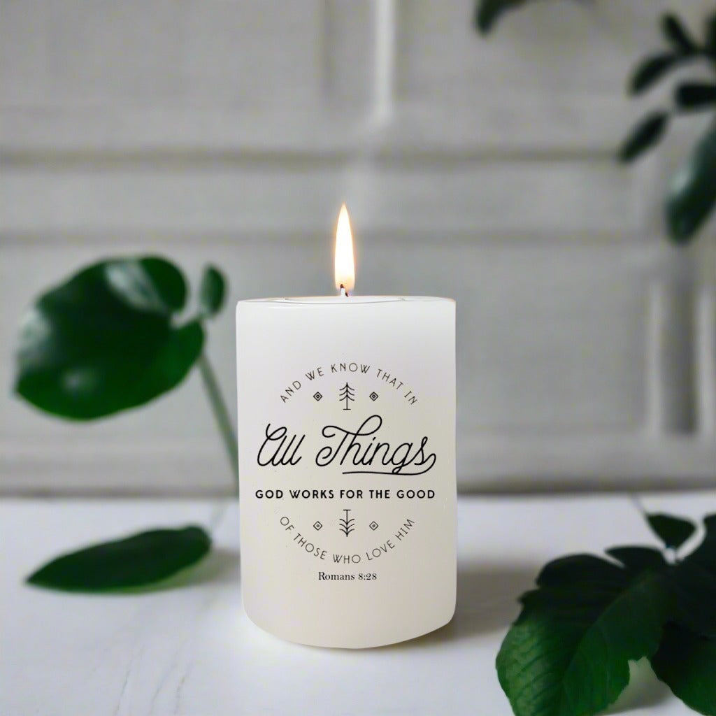 Candle with text design on a white surface with green leaves