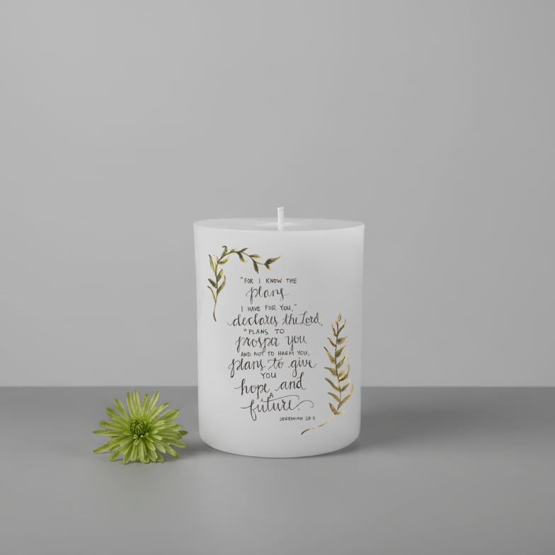 White flattop pillar candle with text and green leaves on a grey background