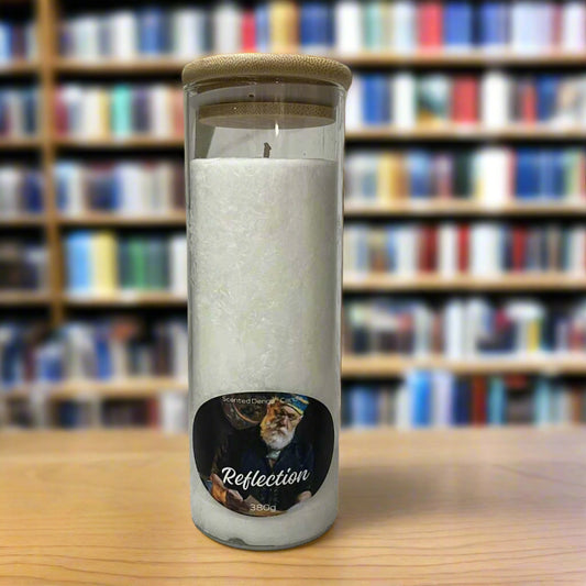 Scented Denga Candle in a glass jar with a wooden lid on a wooden surface, featuring a label with a face and the word 'Reflection'.