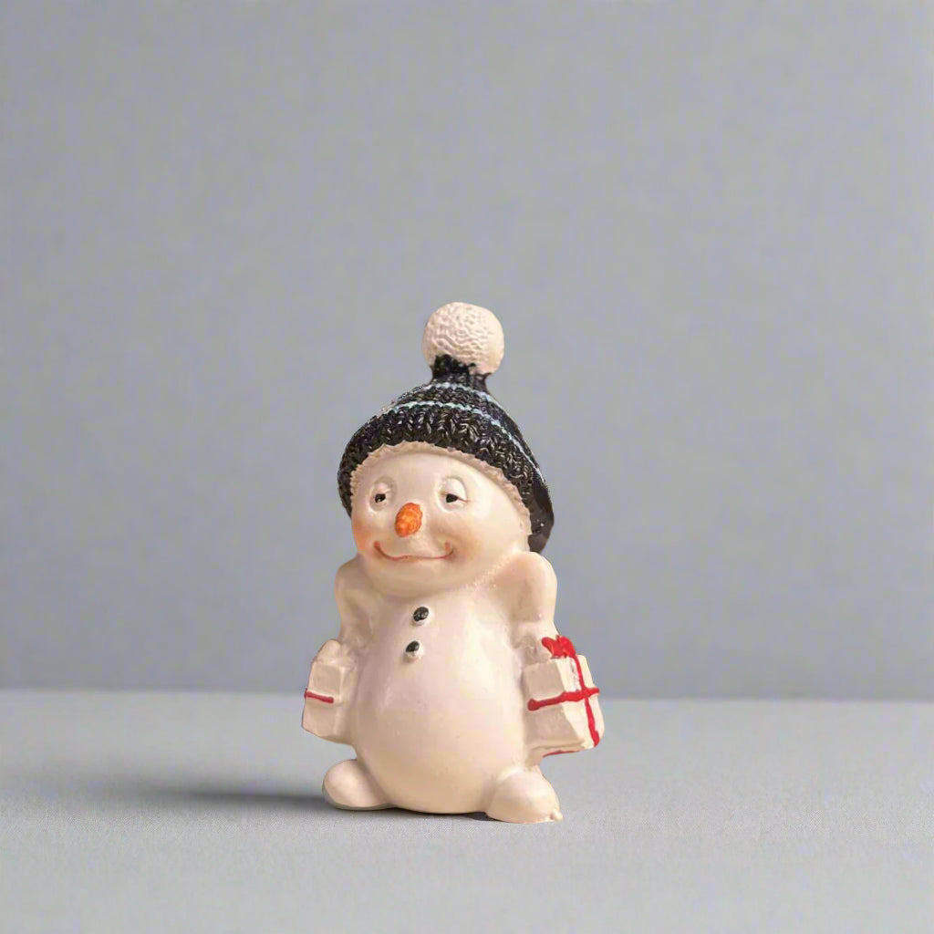 Small snowman figurine with a blue beanie carrying gifts