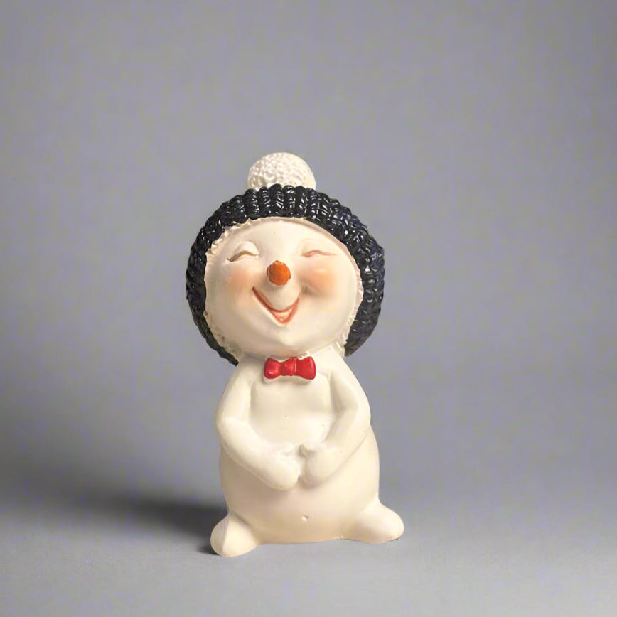 Snowman figurine with a black knit hat and red bow tie on a gray background