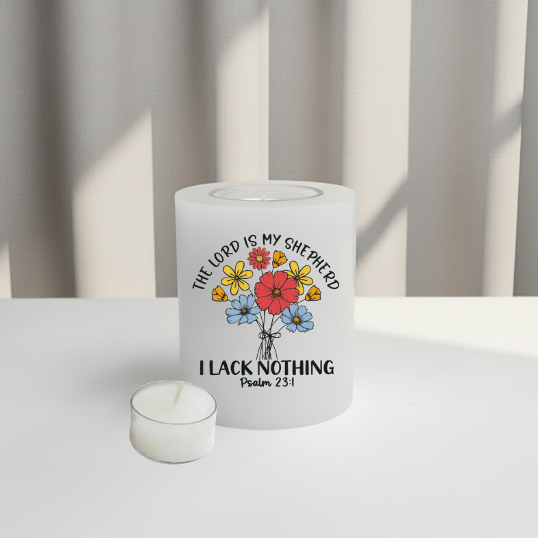 A white candle with a colourful floral graphic and the text 'THE LORD IS MY SHEPHERD I LACK NOTHING Psalm 23:1' printed on the front, set on a white surface.