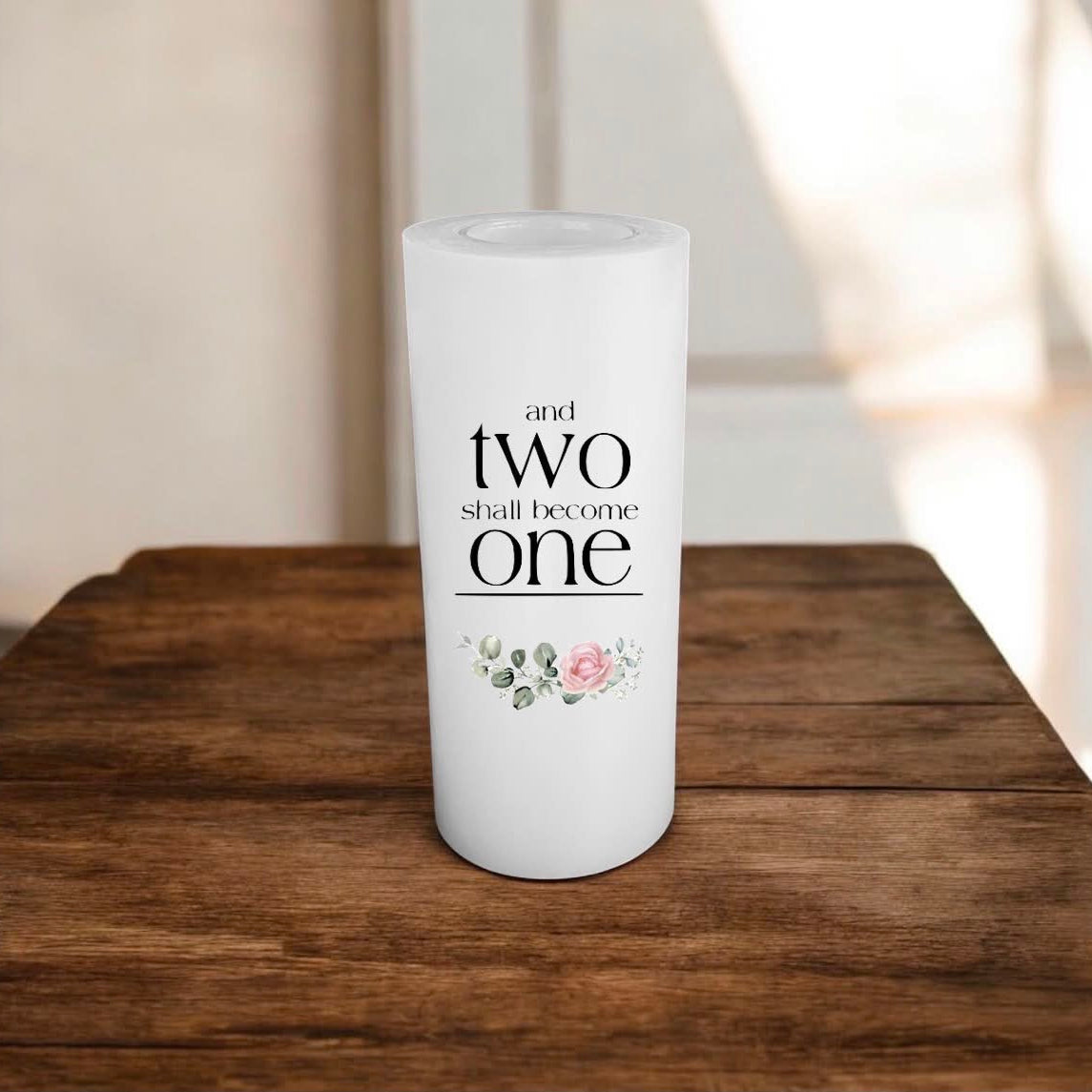 A white candle printed 'and TWO shall become ONE' and a flower