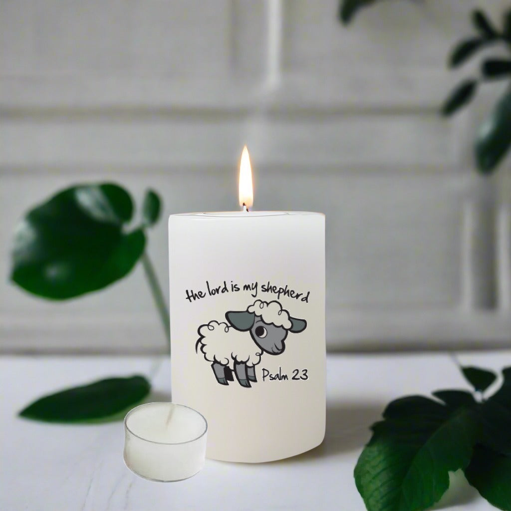 White candle with a sheep illustration and text on a white surface with green leaves.