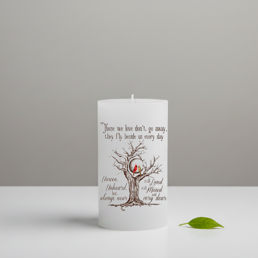 White candle with a tree and bird design on a gray background