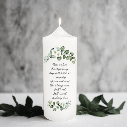 White memorial candle with greenery design and text on a gray background