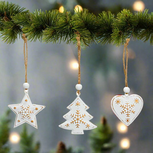 Three white Christmas ornaments shaped like a star, tree, and heart with gold snowflake designs on a white background.