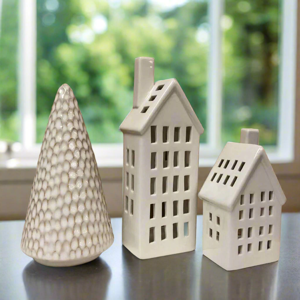 Two ceramic house-shaped and one tree ornaments in front of a window