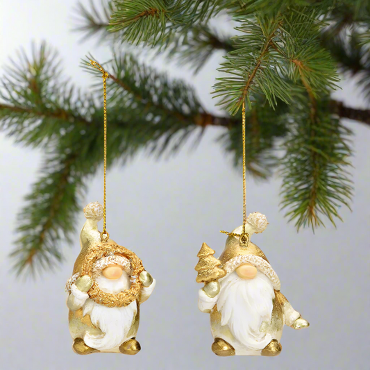 Two decorative gnomes with gold hats and white bodies hanging on a fir branch