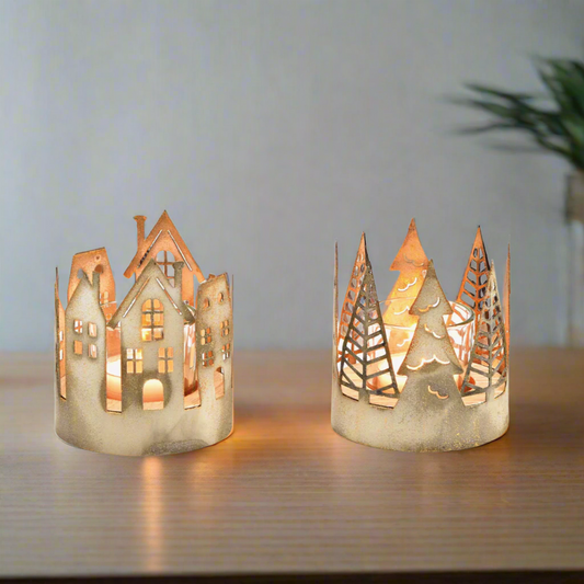 Two decorative candle holders shaped like houses and trees on a white background