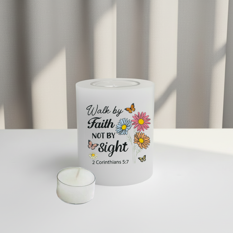 A white glass candle holder with a printed religious quote reading 'Walk by Faith NOT BY sight 2 Corinthians 5:7' alongside colourful illustrations of daisies, buttercups, and butterflies, displayed on a white surface.