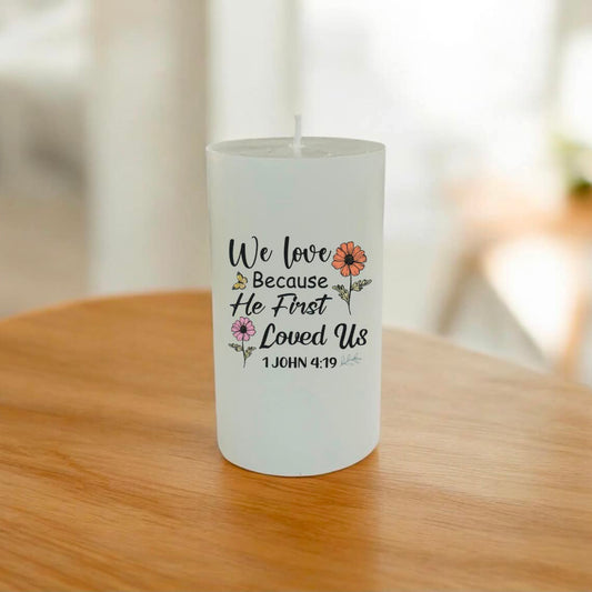 A white pillar candle with a printed sentimental message and small floral illustrations, sitting on a wooden table in a softly blurred indoor setting.