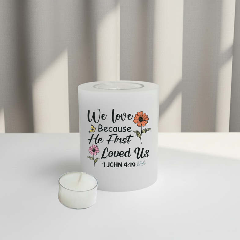 A white candle with a printed message and floral design, sitting on a white surface with soft window light