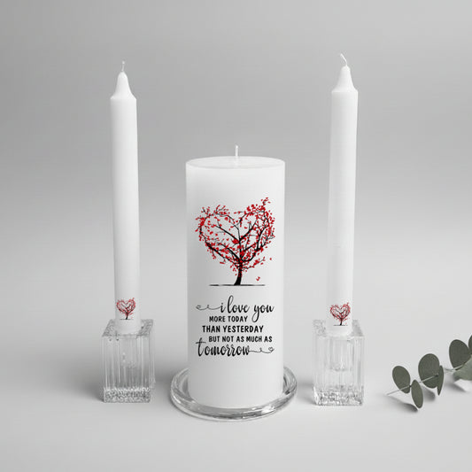 White candle with red heart design and text, flanked by two tall white candles on a light gray background.