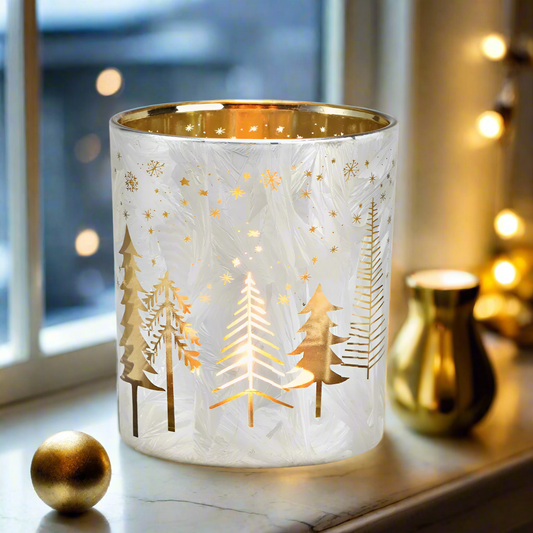 Decorative glass candle holder with gold tree silhouettes on a window sill