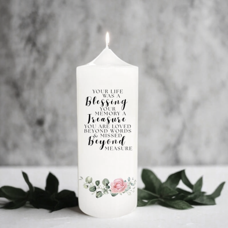 White memorial candle with text and floral design on a gray background