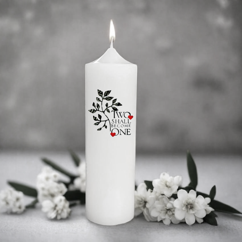 White wedding candle with 'Two Shall Become One' design surrounded by white flowers on a gray background