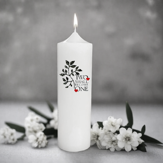 White wedding candle with 'Two Shall Become One' design surrounded by white flowers on a gray background