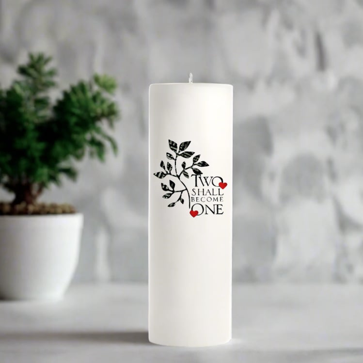 White wedding candle with decorative text and design on a gray surface with a plant in the background