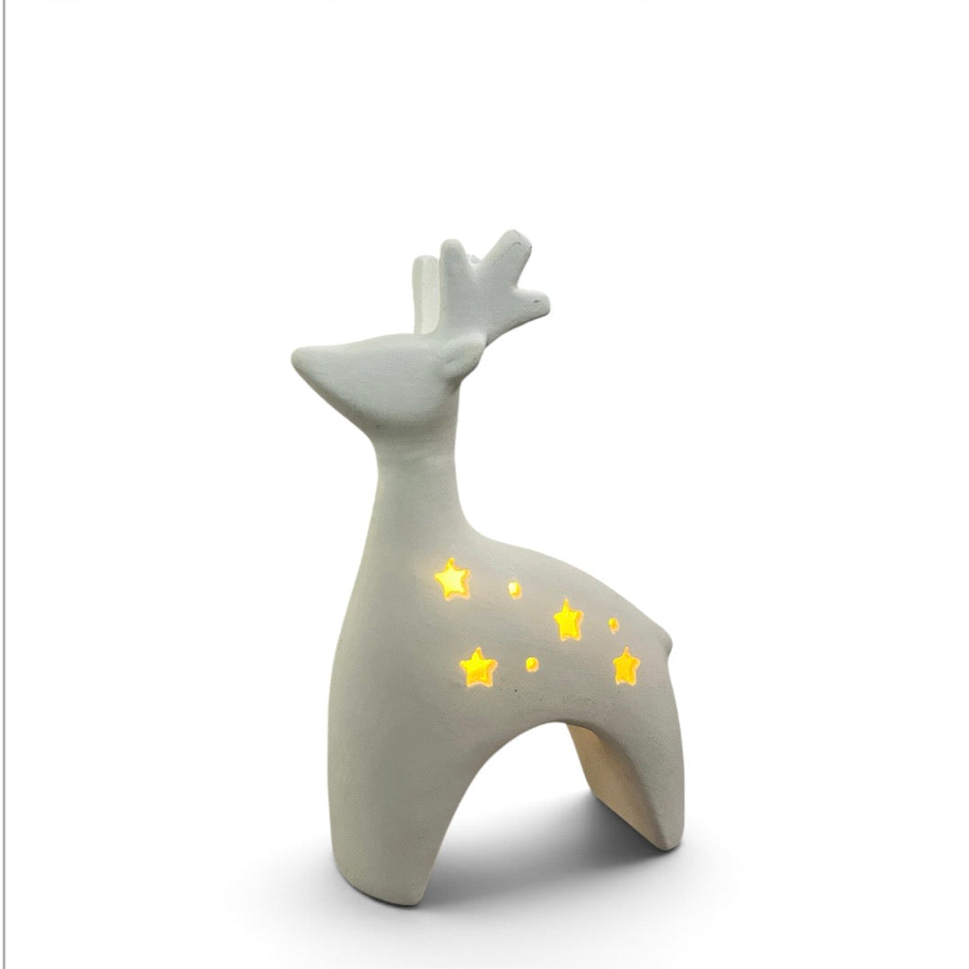 A ceramic deer figurine in a light gray glaze, featuring star-shaped cutouts on its back that glow with warm yellow light