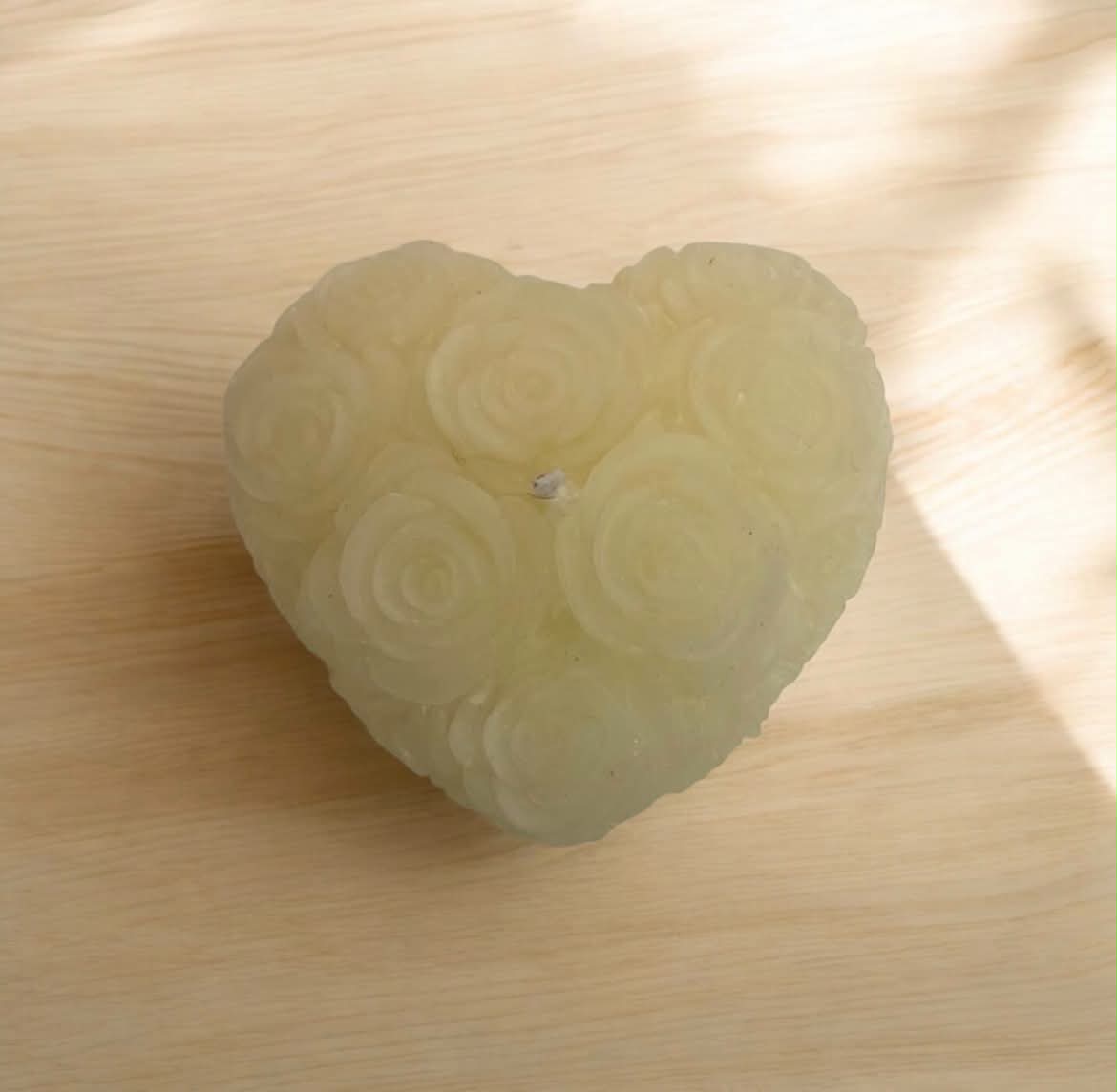 A heart-shaped translucent candle with a carved rose pattern, resting on a light wood surface.