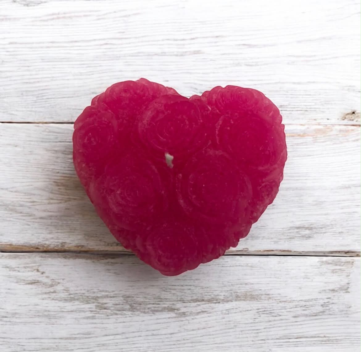 A heart-shaped pink candle with a rose pattern, placed on a white wooden background.