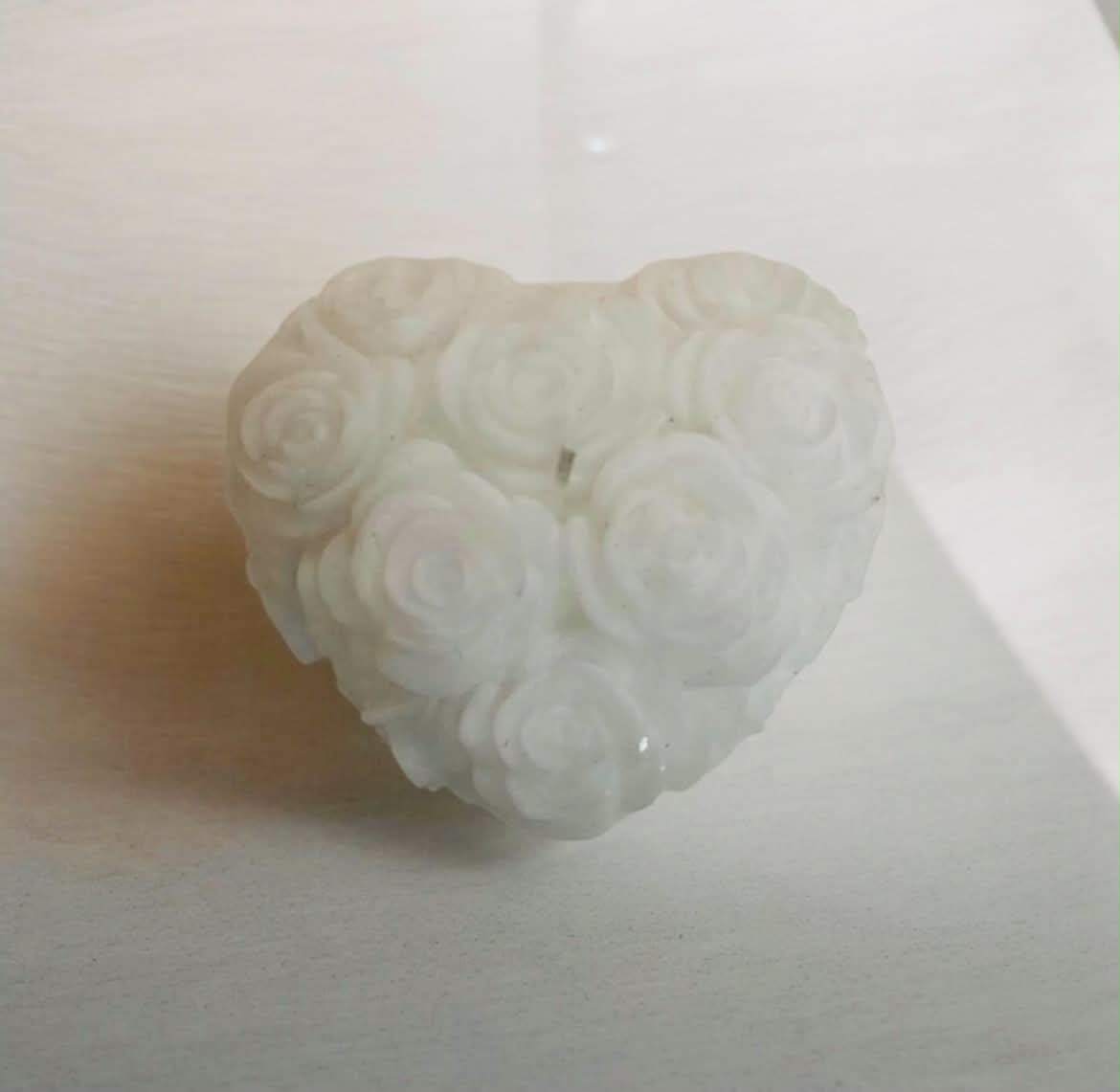 A white carved heart-shaped pendant or ornament featuring a cluster of rose motifs, photographed on a plain light surface.