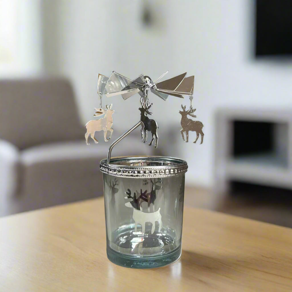 Decorative glass candle holder with metal reindeer charm on a wooden surface.