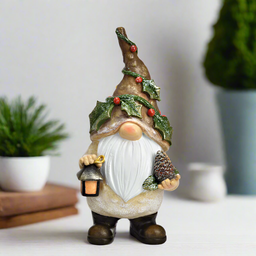 Decorative gnome figure with a hat adorned with holly leaves and berries, holding a lantern and a pinecone