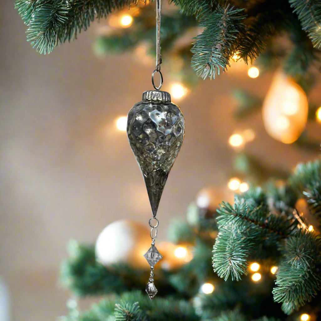Decorative hanging silver glass ornament with crystal-like design on a Christmas tree
