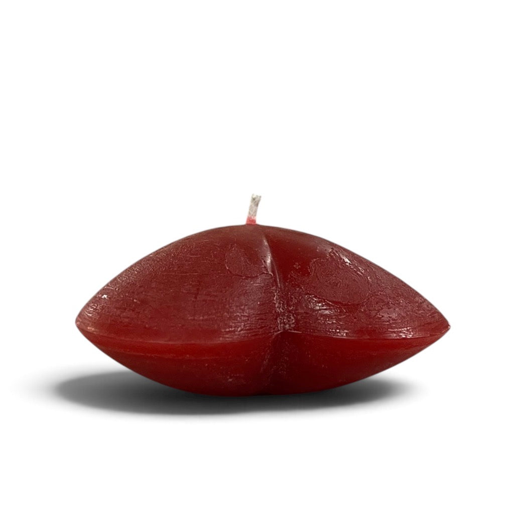 A heart shaped candle placed on a white surface, shown the side view
