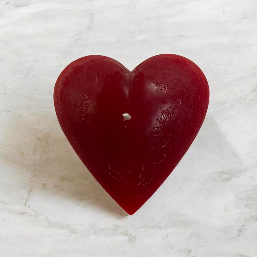 A red heart shaped art candle placed on a marble surface and shown the upper view.