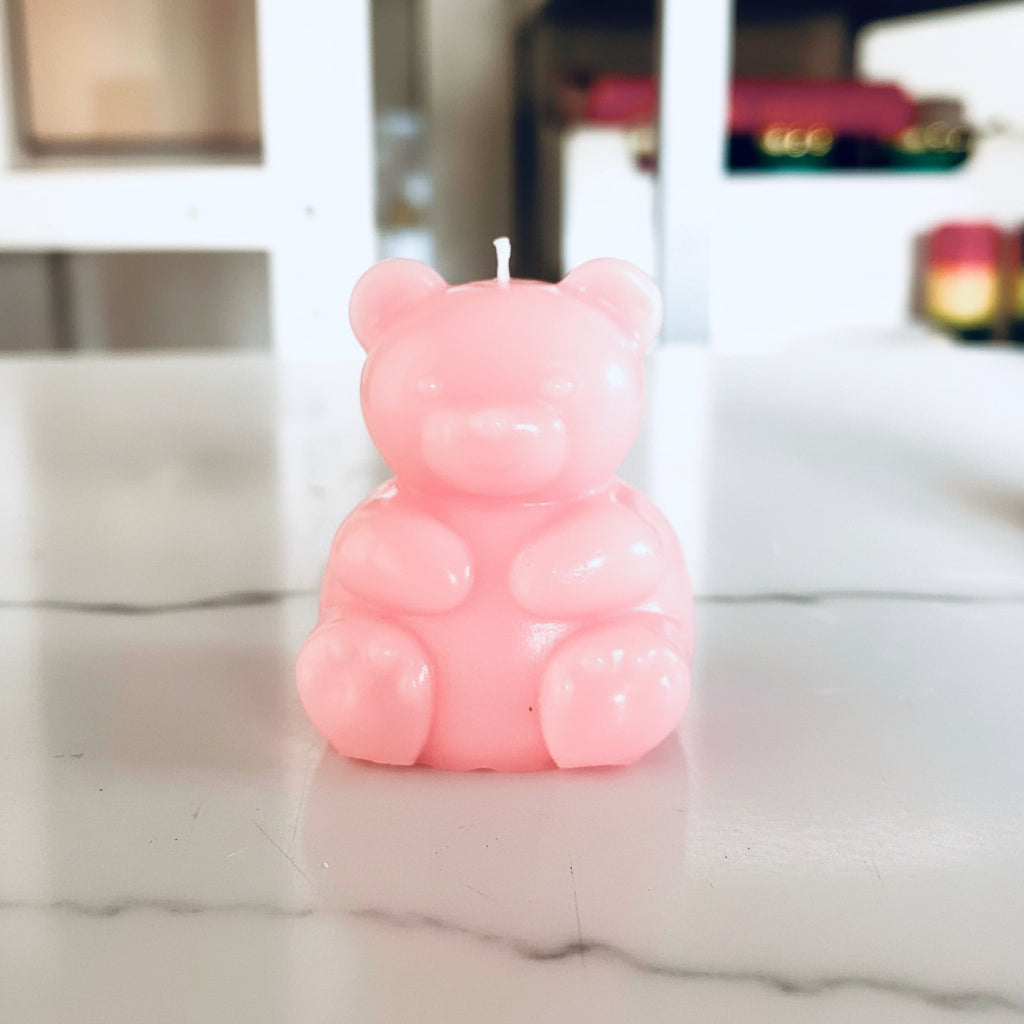 A small rose bear-shaped candle with a wick on top, standing on a light-colored surface with a blurred background.