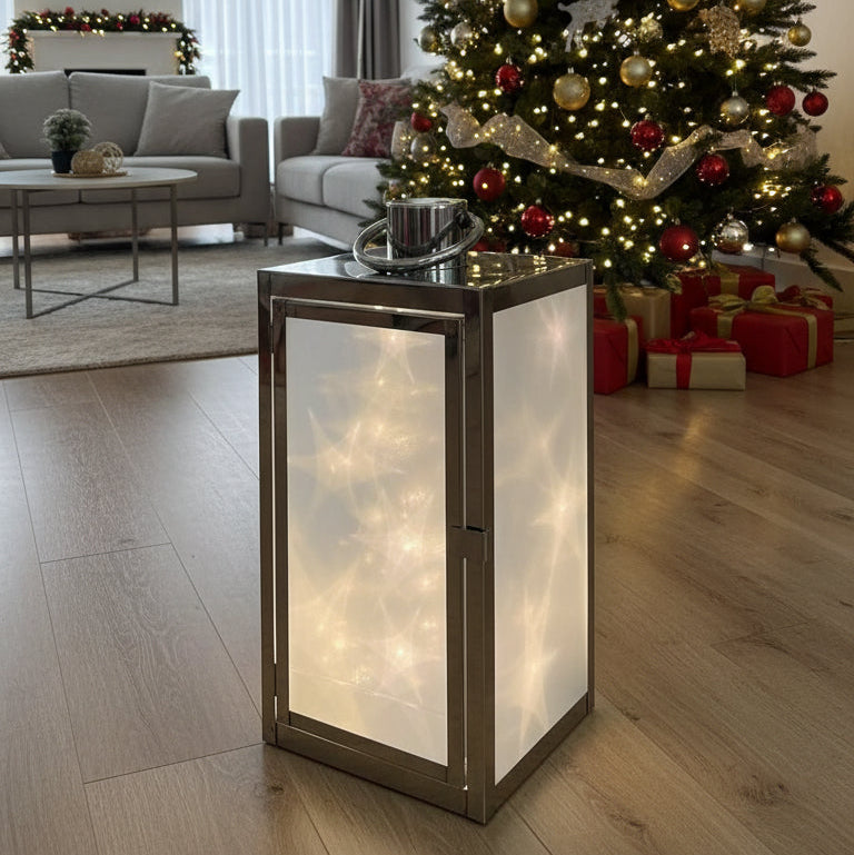 Decorative lantern with star design on a wooden surface in front of a Christmas tree