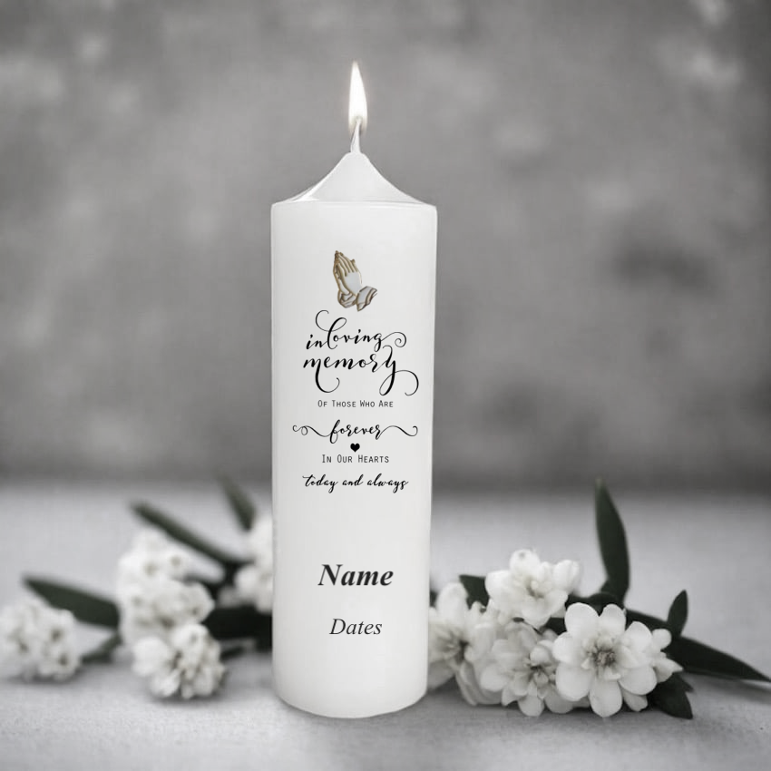White memory candle with engraved text and butterfly design, surrounded by white flowers on a gray background