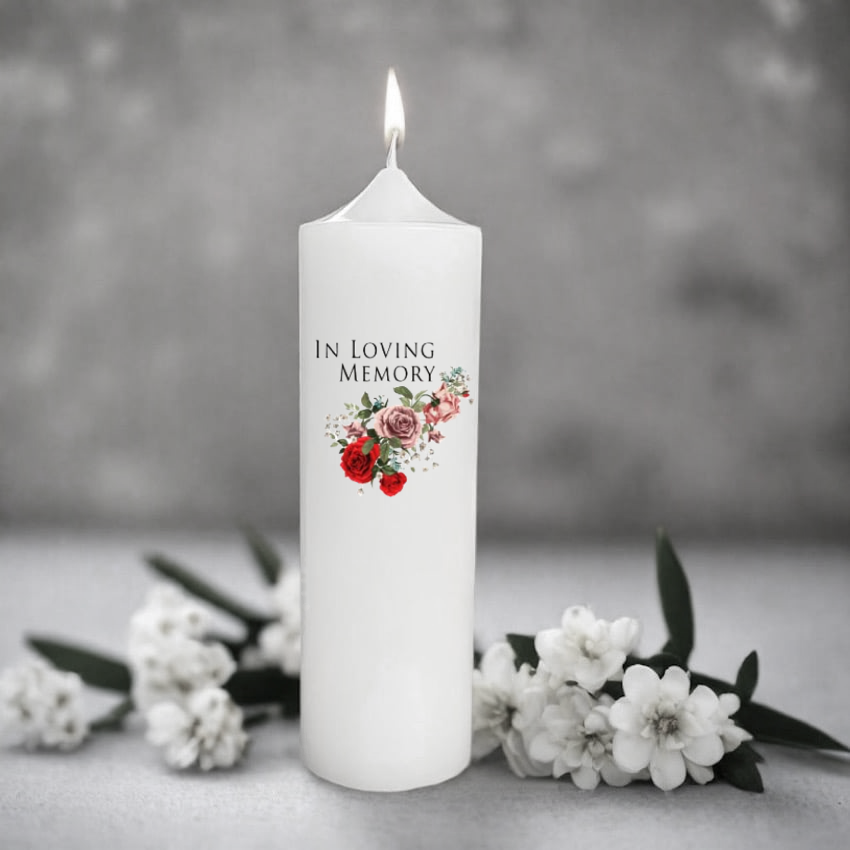 White memory candle with floral design and 'In Loving Memory' text, surrounded by flowers on a gray background