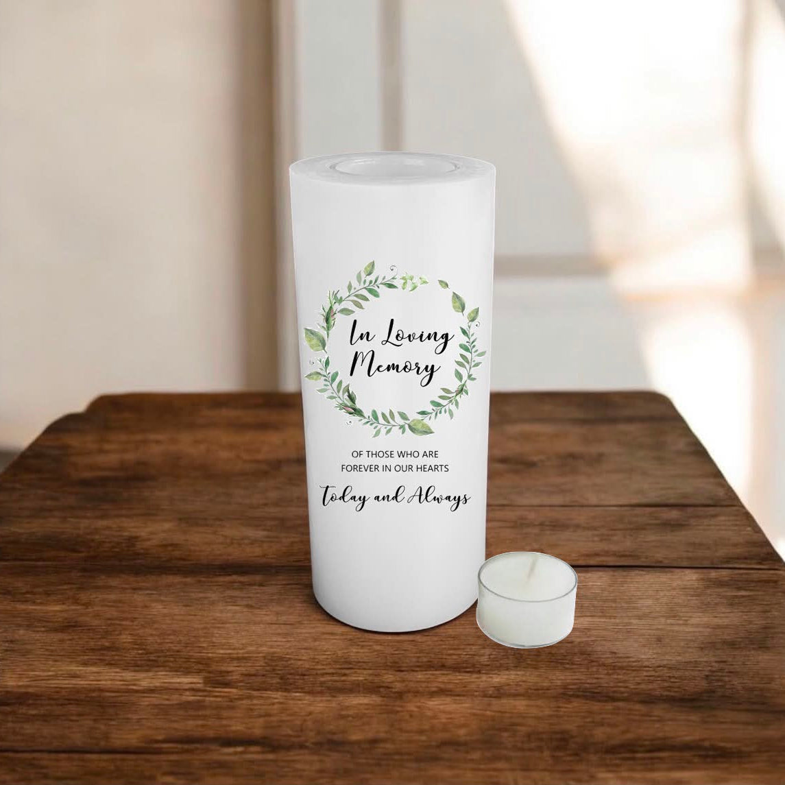 A white candle with a green watercolor wreath design and the text 'In Loving Memory' sits on a rustic wooden table.