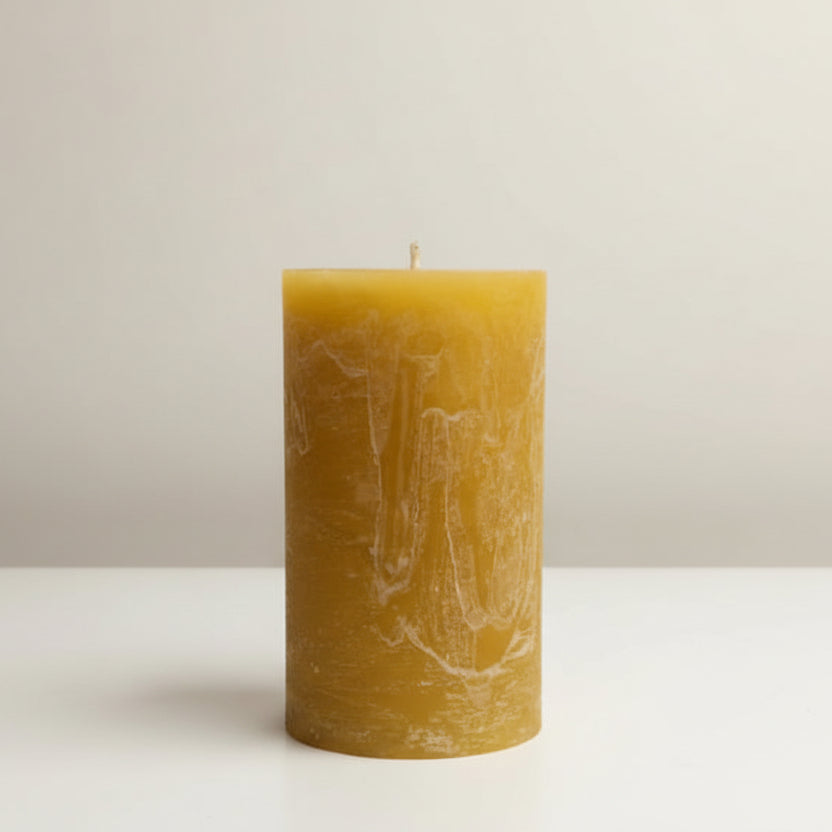 mustard pillar candle on a white surface and a neutral background