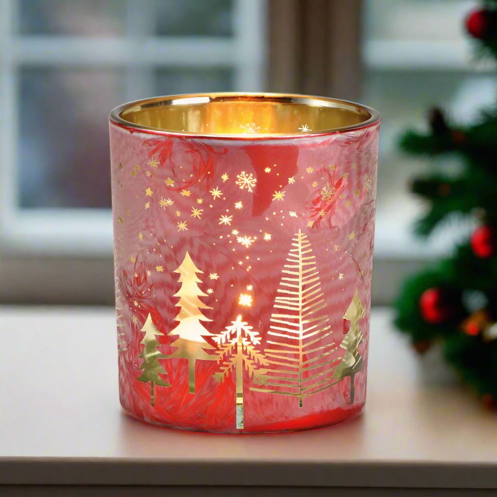 Decorative red glass candle holder with gold Christmas tree design on a window sill