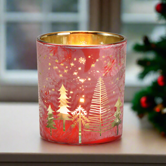 Decorative red glass candle holder with gold Christmas tree design on a window sill