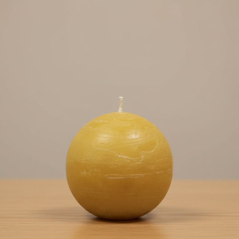 mustard spherical candle on a wooden surface with a beige background
