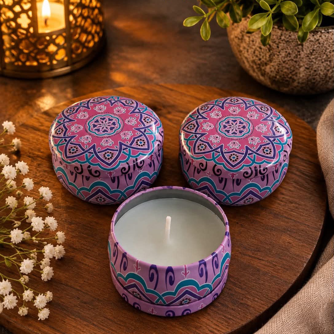 Three small decorative tin candles on a round wooden tray, with two lids shown open and one candle in the front. The tins have a purple, pink, and blue mandala-style pattern.