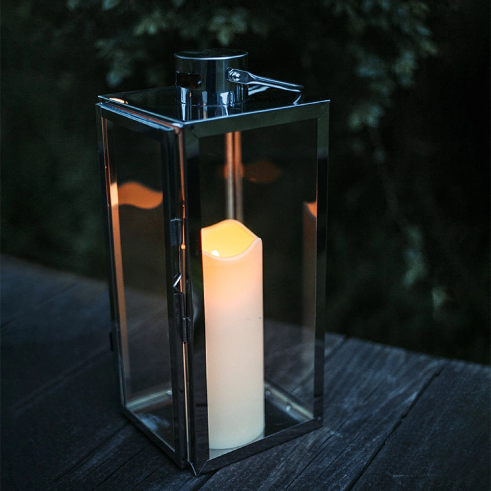 Silver lantern with a lit candle on a wooden surface at night