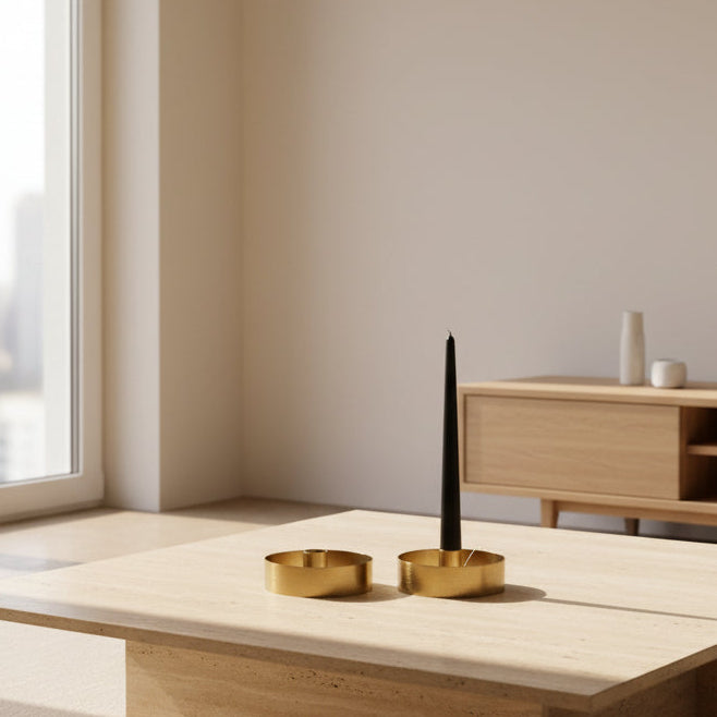 Two brass candle holders with one black candle on a wooden table in a modern living room
