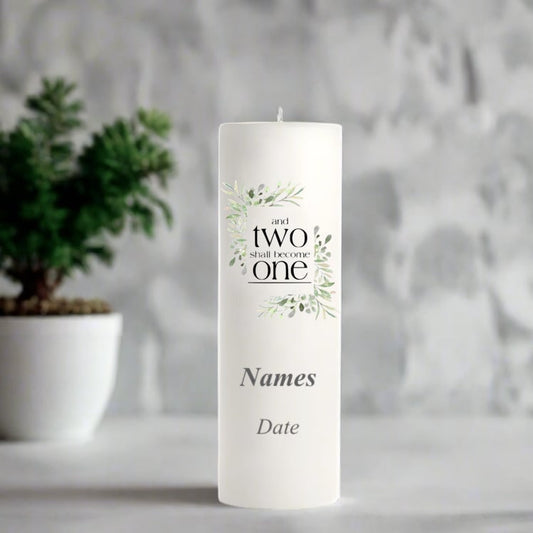 White wedding candle with a decorative label in front of a blurred plant and abstract wall.